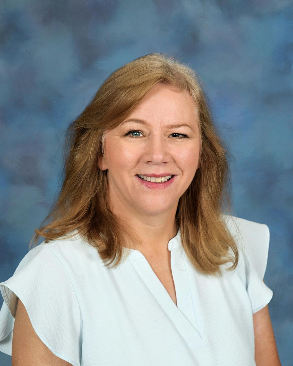 Lady with blonde hair, wearing a smile and a white shirt